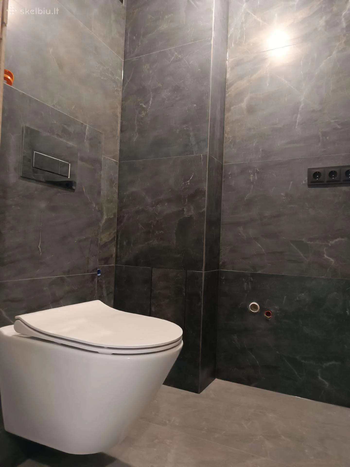 Tamsiai pilkų marmuro efekto didelių plytelių vonios sienos su pakabinamu WC ir chromuotu nuleidimo skydeliu